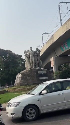 Morning traffic flows past family statue in Dhaka