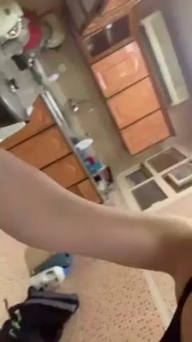 A woman stands in a kitchen and speaks to the camera. She is holding a knife. She shows a dish covered in aluminum foil. She looks at the camera and speaks.