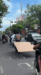 Scooter rider carries large flat material on busy Denpasar street