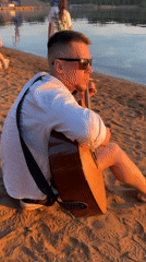 Guitarist watches sunset from beach in golden evening light