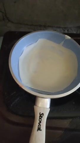 The video opens with a close-up of a light blue frying pan with a white lining, containing a piece of parchment paper. The pan has a light-colored handle with the word "Stoval" in black lettering. The pan is on a black stovetop. The scene then shifts to a wider shot of a metal wok filled with chopped ingredients, appearing to be potatoes and carrots, being stirred with a metal spoon and a spatula. The ingredients are being cooked. The video briefly returns to the frying pan and parchment paper before ending.