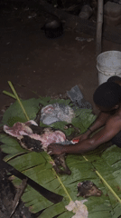 Man butchers animal carcass outdoors at night in Eziudo