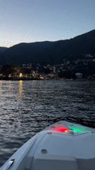 White boat navigates dusk waters past an illuminated hillside town