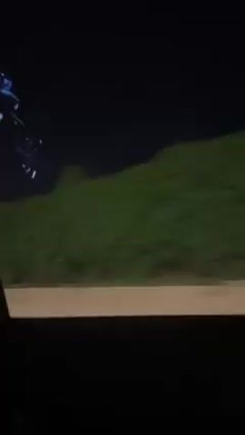 The video shows the inside of a car at night, the camera moving from the window to the interior, showing the back of the driver's head, the rearview mirror, and the various electronic displays on the dashboard. The car is moving along a road next to greenery, and some streetlights are visible.
