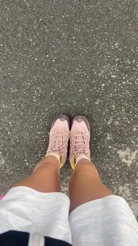 This media file features a person's legs in hiking shoes, standing on asphalt. The scene then transitions to a picturesque view of a village nestled in a valley, with snow-capped mountains in the background. The village has traditional Swiss architecture with wooden houses and tiled roofs. Cable cars and power lines are visible, indicating a developed area within a mountainous region. The sky is partly cloudy, suggesting a mixed weather day. The overall mood is one of exploration and appreciation for natural beauty. There is no visible text in the media.