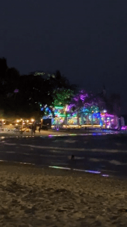 Colorful lights reflect on water at Thailand beach night
