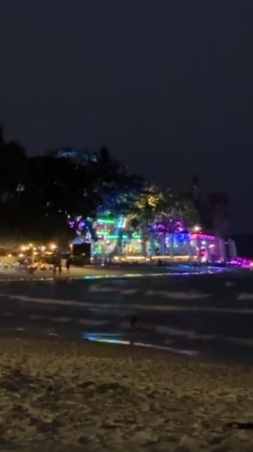Colorful lights reflect on water at Thailand beach night