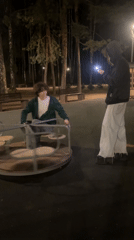 Two friends play on merry-go-round at night in Saint Petersburg