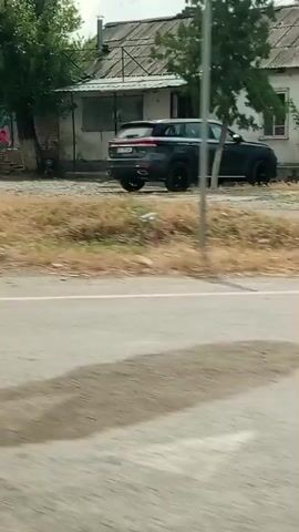A video shows a yellow portable generator with a blue umbrella over people sitting near it. A white car is parked to the left. The video then shows a brick wall and trees. The next clip shows a white SUV parked at a red and white building, with people near the vehicle. The video continues to show gas pumps at a station. Finally, it shows a gas station sign and pumps with a white fence. The video appears to have been filmed from a moving vehicle.