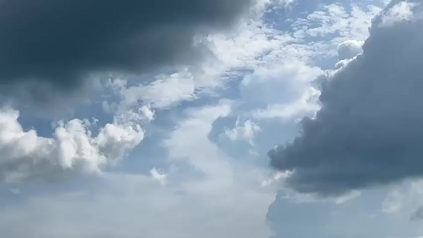 The video shows a cloudy sky. There are both dark storm clouds and lighter, fluffy clouds in the frame.  Some blue sky is visible between the clouds.