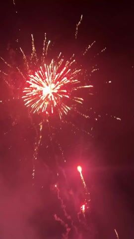 Fireworks are set off in the night sky, creating bursts of red, gold, and green light. Smoke from the explosions fills the air.