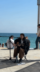 Street musician performs as pedestrians pass Barcelona waterfront