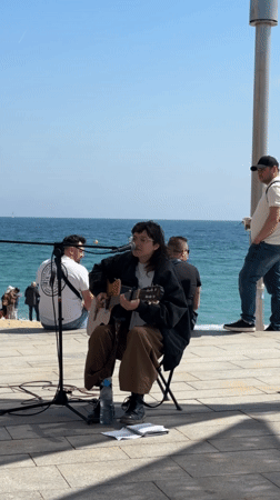 Street musician performs as pedestrians pass Barcelona waterfront