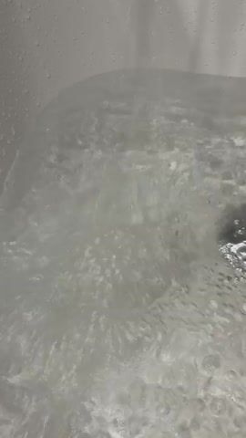 The video shows a close-up, overhead view of water boiling vigorously in a white sink or bathtub. Bubbles are rapidly rising to the surface, and the water appears turbulent and steamy. The sides of the sink or tub are visible, with water droplets clinging to the white surface. The lighting is bright, illuminating the chaotic motion of the boiling water.