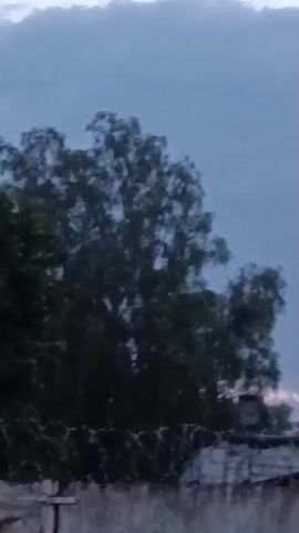 A still image captures a silhouetted chimney against a twilight sky with scattered clouds. To the left, the upper branches of a dark tree are visible, and the edge of a rooftop extends across the bottom of the frame. The overall scene is dark and appears to be outdoors.