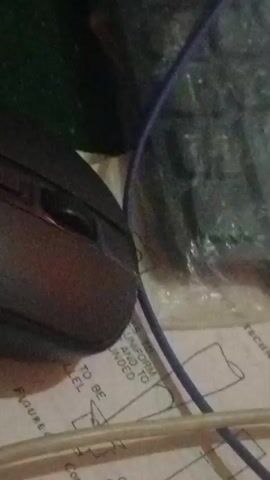 The video is a close-up shot of a black computer mouse resting on a piece of paper with text and diagrams. The paper appears to be from a book or manual, with visible text and schematic drawings. A blue wire and a white cable are also present in the frame, partially obscuring the mouse and paper. The lighting is dim, and the image quality is slightly grainy. There are no people visible in the video.