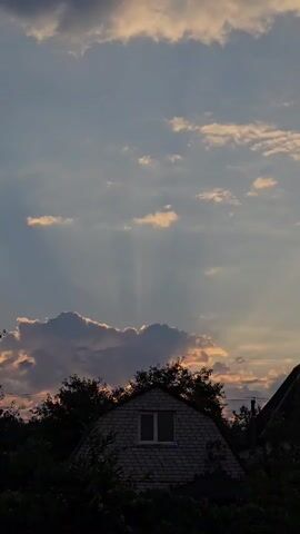 A time-lapse video shows a sky with clouds and sunbeams passing over a house and trees.