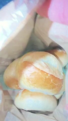A person's hand reaches into a brown paper bag filled with bread rolls. The rolls appear to be golden brown on top. The background is blurred.