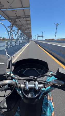 Scooter riders cross Denpasar bridge as plane flies overhead