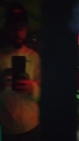 The video appears to be taken inside an indoor playground or play structure. There are areas with red and green lighting, possibly from colored light fixtures or panels. The structures look padded and are a mix of materials, including netting. A person is briefly seen holding a smartphone, possibly taking a selfie or filming the environment. The overall impression is of a brightly colored, slightly blurry, and perhaps disorienting indoor play area.