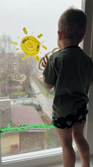 Toddler paints window while standing on sill in Rusanovo