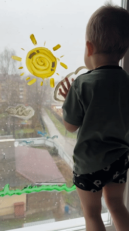 Toddler paints window while standing on sill in Rusanovo