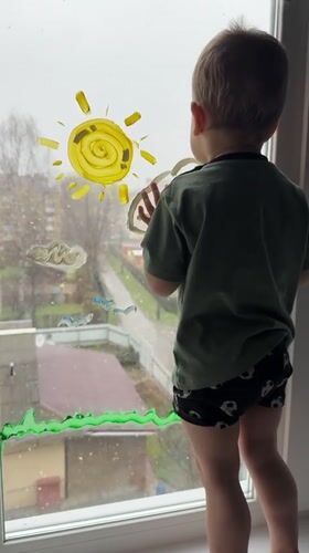 Toddler paints window while standing on sill in Rusanovo
