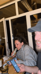 Women sing karaoke indoors with group around wooden table