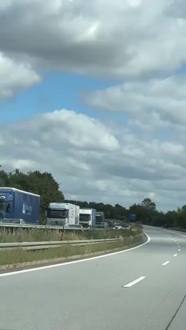 A truck is seen driving on a highway under a cloudy sky.