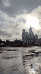 Wet cobblestone plaza fronts a domed white building in Hrodna
