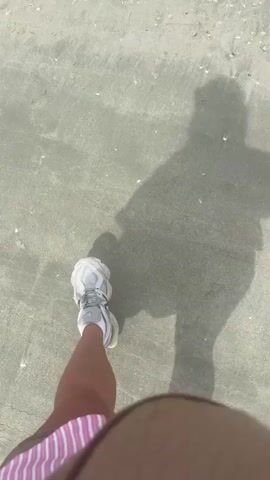 The video begins with a shadow of a person walking on a sandy beach. The person is wearing sneakers and a striped cloth. The camera pans up to show the ocean and the sky. There are two people in the water in the distance. The video ends with a view of the ocean and the beach.