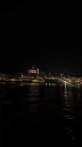 The media file shows a nighttime view of a city skyline across a body of water. The most prominent subject is a large, illuminated building with a dome and a tall spire, likely a cathedral or important landmark. The city is dotted with numerous lights, indicating a populated area. The water in the foreground reflects the city lights, creating shimmering patterns on its surface. The sky is dark, signifying nighttime.

The scene appears to be a picturesque cityscape, possibly a historic European city given the architecture of the central building. The lighting suggests it is a clear night, with no visible signs of rain or fog. The location cues point to Sliema, Malta, suggesting the view is likely of Valletta.

The overall emotion conveyed is one of tranquility and beauty, characteristic of a nighttime city view. The activity taking place is the passive observation of the illuminated city from across the water. There is no visible text in the media file.