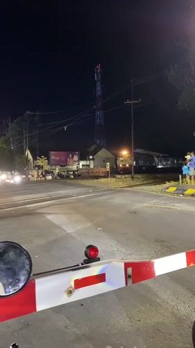 Train crosses through Madiun intersection as gates lower, traffic waits
