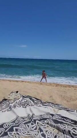 The video captures a sunny day at a beach in Premià de Mar, Spain. In the initial frame, a patterned blanket with a shoe on it is visible in the foreground on the sand. Beyond, a person, partially seen, stands at the water's edge, seemingly throwing an object into the sea. The blue-green ocean stretches out under a clear blue sky, with gentle waves lapping the shore.

The scene then zooms in on a black and white dog, resembling a Border Collie, that runs into the shallow water. The dog swiftly retrieves a purple frisbee from the breaking waves. Holding the frisbee firmly in its mouth, the dog happily trots back onto the sandy beach. The clear weather and calm sea suggest a pleasant day for outdoor activity. No visible text is present in the video.