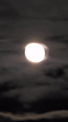 Full moon observed through passing clouds on evening