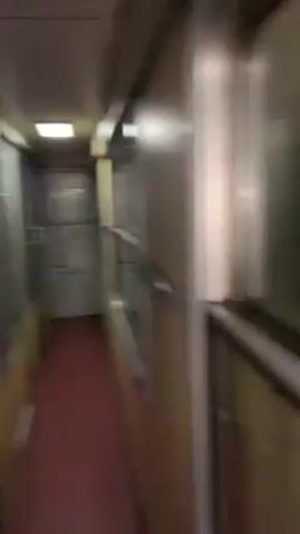 The video shows the inside of a subway car moving through a tunnel. The interior is a pale yellow, with silver trim around the windows and doors. The floor is maroon, with a white arrow taped to it. In the distance, one can see an orange object, and a fire extinguisher in a recessed compartment on the wall. The camera moves smoothly forward along the aisle.