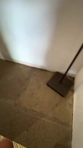 The video shows a person's feet, wearing white sneakers, descending a wooden staircase. The staircase is illuminated by ambient light, and the walls appear to be painted white. The camera pans and moves downwards, capturing the steps as the person descends. The video ends as the person reaches what appears to be the bottom of the staircase, where a doorway is visible. The environment seems to be an interior space, possibly a house or a building with a rustic aesthetic. There is a sense of motion and perspective shift as the camera follows the descent.