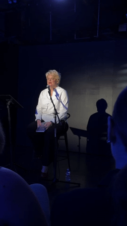 Reading from a book on a bare stage in Los Angeles
