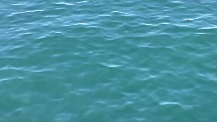 The video shows a close-up view of turquoise-colored water with small waves rippling across its surface. The lighting suggests it is daytime, with sunlight reflecting off the water. There are no people or objects visible in the frame. The camera appears to be stationary or moving very slowly, capturing the continuous movement of the water.