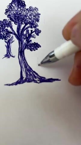 A close-up, top-down shot shows a hand holding a white pen and drawing on a white surface. The pen tip is visible, making blue ink marks. The drawing depicts a tree with a thick trunk and a full canopy of leaves. Another smaller tree is drawn behind the main tree. The pen is currently drawing grass-like strokes near the base of the tree.