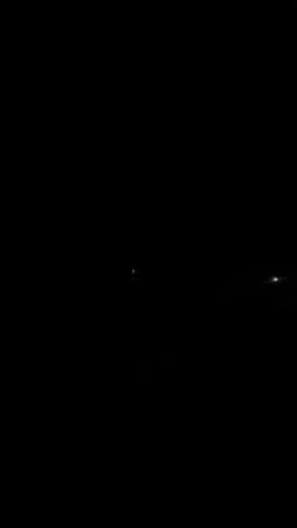 The video is extremely dark, with only faint, distant lights visible. It is difficult to discern any specific objects or people. The lights appear to be very far away, possibly in a city or a rural area. There are no discernible actions or interactions occurring in the video. The environment appears to be outdoors, given the presence of distant lights that might indicate artificial illumination. However, the overwhelming darkness makes it impossible to provide further details about the setting. The overall impression is one of emptiness and obscurity.