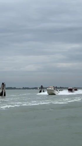 Three motorboats navigate Venice channel under grey skies
