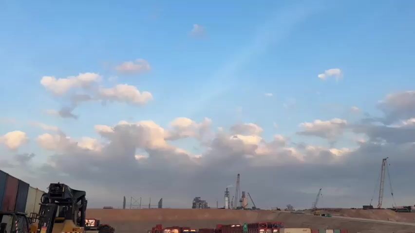 The video shows a construction site with cranes, shipping containers, and heavy machinery under a cloudy sky.