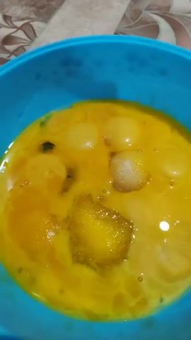 This is a close-up, first-person point-of-view video of several raw egg yolks in a blue bowl. Some of the yolks are intact, while others are broken and mixed with the egg whites. There appear to be small bubbles and some crystallization or clumping of the egg mixture. The lighting is dim and appears to be artificial.