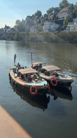Two motorboats docked on the Neckar, Heidelberg hillside behind