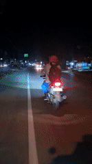 Motorcyclist in red helmet rides dimly lit road in Indonesia