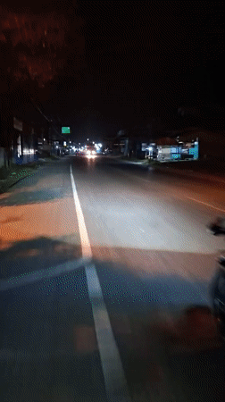 Motorcyclist in red helmet rides dimly lit road in Indonesia
