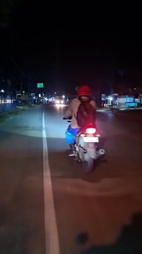 Motorcyclist in red helmet rides dimly lit road in Indonesia