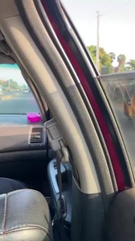 The video shows a view from inside a car as it drives down a road on what appears to be a sunny day. We see views of the passing scenery including trees, buildings, walls, and a few glimpses of other vehicles and pedestrians. The camera is positioned towards the passenger side of the car.