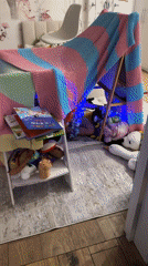 Child plays in illuminated blanket fort with stuffed animals
